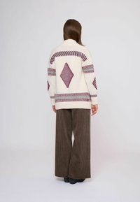 Maglione a maglia bianco sporco con motivo a rombi in bordeaux. Presenta un collo alto e maniche ampie, abbinato a pantaloni in velluto a costine marroni.