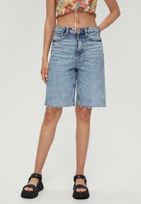 Pantalones cortos de mezclilla azul claro, con cintura alta, corte recto, dobladillo sin rematar y cinco bolsillos. Combinados con sandalias negras de plataforma.