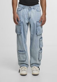 Lysblå denim cargo bukser med flere sidelommer, en afslappet pasform og synlige sømdetaljer. Bæres med hvide sneakers.