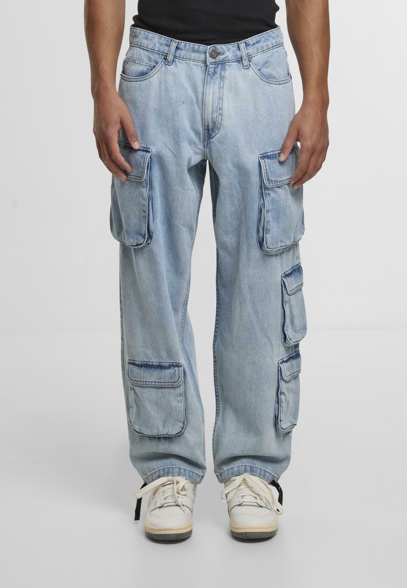 Lysblå denim cargo bukser med flere sidelommer, en afslappet pasform og synlige sømdetaljer. Bæres med hvide sneakers.