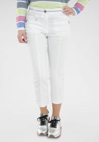 Witte cropped broeken met voorzakken en een strakke uitstraling. Gecombineerd met zilveren sneakers en zwarte veters. Model draagt een gestreepte top.