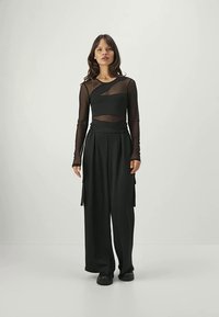 Zwarte lange mouw top met doorzichtige panelen en gelaagd ontwerp, gecombineerd met een broek met wijde pijpen. Beiden hebben een gladde textuur en een minimalistische stijl.