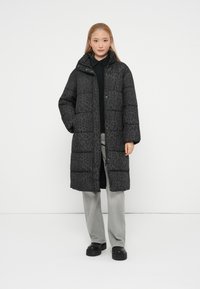 Crni puffer kaput s leopard uzorkom, s patentnim zatvaračem i kopčanjem, visokim ovratnikom i bočnim džepovima. Nosi se preko sivih hlača i platformskih cipela.