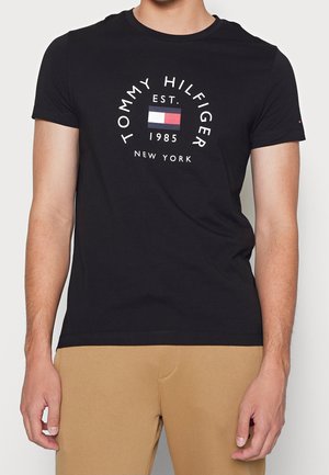 Black cotton t-shirt, short sleeves, featuring a circular white graphic with "TOMMY HILFIGER EST. 1985 NEW YORK" and a colored flag emblem.