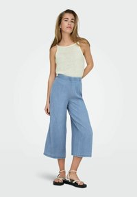 Top de tirantes acanalado verde claro combinado con culottes de mezclilla azul claro de pierna ancha y sandalias planas negras con correas blancas.