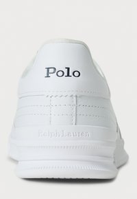 White sneaker with smooth leather upper, featuring embossed "Polo" logo, textured accents, and a rubber sole. Minimalist design details.