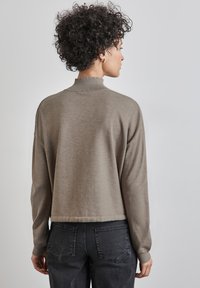 Maglione morbido di un marrone chiaro, con colletto alto e lunghezza cropped. Fit rilassato, maniche lunghe, abbinato a jeans grigi scuri.