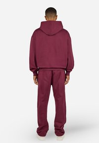 Burgundy hoodie with a loose fit and a large back pocket, paired with matching elastic-waist trousers. Smooth fabric and ribbed cuffs.