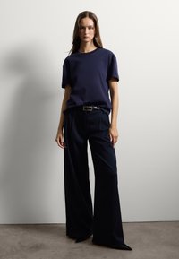 Maglietta blu navy abbinata a pantaloni scuri a gamba larga con vita alta. Cintura con fibbia metallica. Tessuto liscio con vestibilità rilassata.