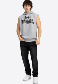 Gray sleeveless hoodie with black lion graphic and "Lonsdale London" text, paired with dark jeans and white sneakers. Simple design.