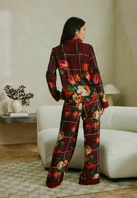Floral-printed pajama set in burgundy plaid, featuring large colorful flowers, collar, and long sleeves. Loose-fit pants with similar pattern.