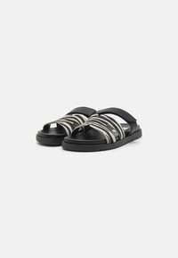 Zwarte sandalen met twee gestreepte stoffen banden in wit en beige, en een rubberen zool met textuur. Openteenontwerp met een verstelbare pasvorm.