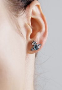 Sapphire stud earring with a silver base, featuring a floral design. The gemstone is oval, surrounded by smaller clear stones, adding sparkle.
