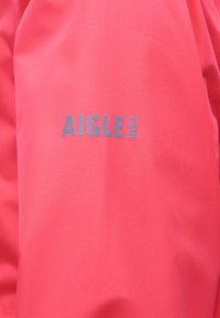 Tissu corail lumineux avec texte argenté centré "AIGLE 1853" imprimé dessus.