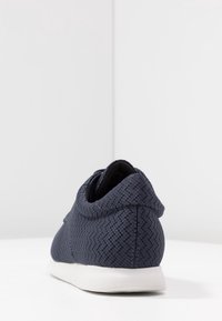 Mörkblå sportskor med en strukturerad tygöverdel, vit mellanlägg, och rund häl, med snörningsdesign och vadderad krage.