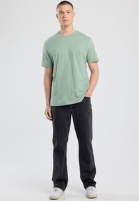 Light green short-sleeve t-shirt paired with black jeans. The shirt is crew-neck and made of soft fabric, with a relaxed fit. White sneakers.
