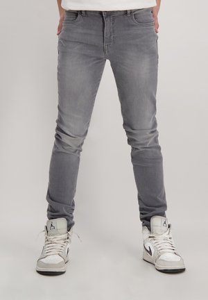 Grijze slim-fit jeans met een gladde textuur, voorzien van een klassieke vijf-pocketontwerp en subtiele vervaging. Gecombineerd met witte hoge sneakers.