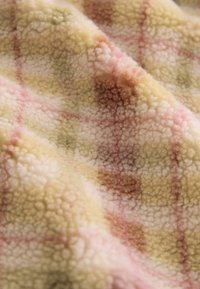 Fuzzy fleece stof i gul med et ternet mønster, der har pink og grønne accenter. Blød tekstur med en let glans og subtile farvevariationer.