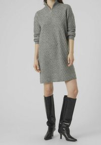 Robe grise en tricot avec un col montant et un motif côtelé diagonal ; associée à des bottes noires brillantes à talons montant jusqu'au genou.