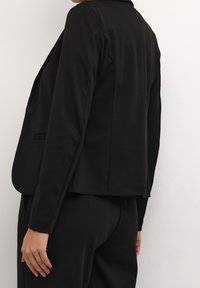 Schwarzer Blazer aus weichem Stoff, mit strukturiertem Design, flachen Revers und Ein-Knopf-Verschluss. Der Rücken ist leicht verkürzt.