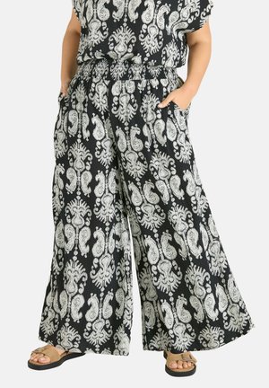 Czarne spodnie z szerokimi nogawkami z misternym białym, kwiatowym wzorem paisley, elastyczna talia, boczne kieszenie, w połączeniu z beżowymi sandałami.