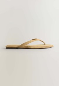 Sandale tong en daim beige avec fines brides et semelle noire basse, présentée de profil sur un fond clair.