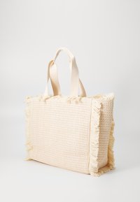 Textured beige tote bag with fringed edges, soft fabric, and sturdy handles. The design is rectangular with a relaxed shape.