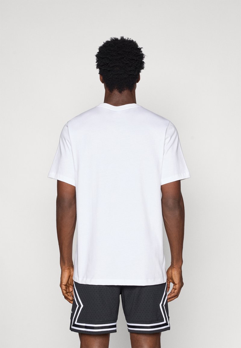 T-shirt blanc à manches courtes avec un col rond, associé à un short de sport noir avec une texture en maille et des accents en blanc.
