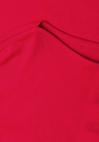 Tissu rouge vif avec des plis superposés et des détails de couture visibles sur une surface lisse et texturée.