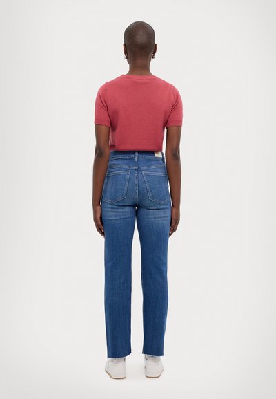 Top de punto corto de manga corta en rojo combinado con jeans de denim azul de tiro alto, que cuentan con cinco bolsillos y un corte recto. Zapatillas blancas completan el conjunto.