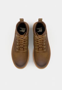 Bottines en cuir marron avec un bout arrondi, un design à lacets, des œillets en métal, des coutures contrastées et une languette à l'arrière.