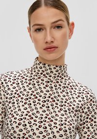 Kremowy golf w print leopardzi, z czarnymi i czerwonymi akcentami, prążkowaną fakturą oraz dopasowanym krojem.