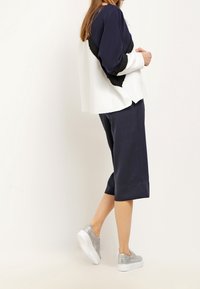 Top v námořnické a bílé barvě se černými akcenty, spárovaný s tmavě námořnickými kalhotami po kolena a stříbrnými teniskami. Měkká tkanina a volný střih.