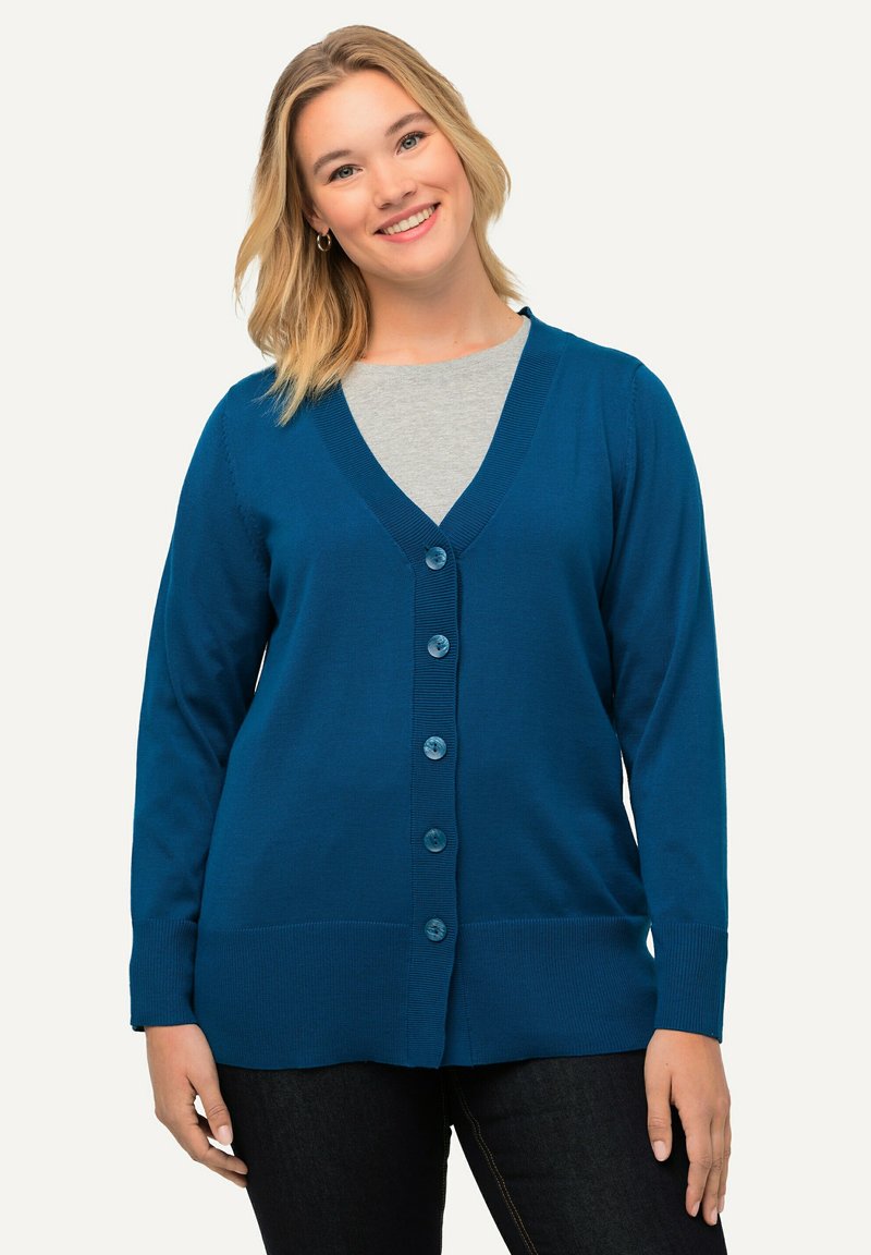 Turkos cardigan med V-ringning, fem stora knappar och ribbade ärmar. Bärs över en ljusgrå topp med en slät stickad textur.