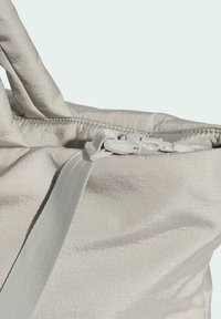 Lysegrå taske med en glat, tekstureret overflade. Har en hvid lynlås og strop, med et vinklet design, der fremhæver minimalisme.