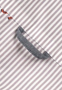 Tissu rayé gris et blanc avec un petit détail de boucle tissée gris foncé et deux minuscules motifs de papillons orange près de la couture.