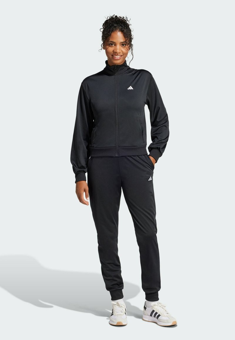 Schwarzer sportlicher Trainingsanzug mit Reißverschlussjacke und passender Hose. Merkmale sind gerippte Bündchen und Taillenbund, schwarzer Stoff und weiße Logoakzente.