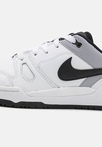 Baskets blanches et grises avec une tige en cuir texturé, des accents noirs, des lacets blancs plats et une semelle en caoutchouc noire. Présente un logo swoosh central.