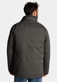 Donkergroene gewatteerde jas met een hoge kraag, zijzakken en een gladde textuur. Voorzien van een rits en minimale stikdetails.