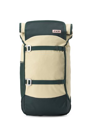 Beiger und dunkelgrüner Rucksack mit Rollverschluss, zwei verstellbaren Riemen auf der Vorderseite und einem kleinen rosa Etikett nahe der oberen Mitte.