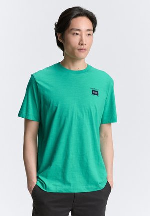 Zeleni bombažni T-shirt s krojnim ovratnikom, kratkimi rokavi in majhno blagovno oznako na prsih. Gladka tekstura, sproščen kroj.