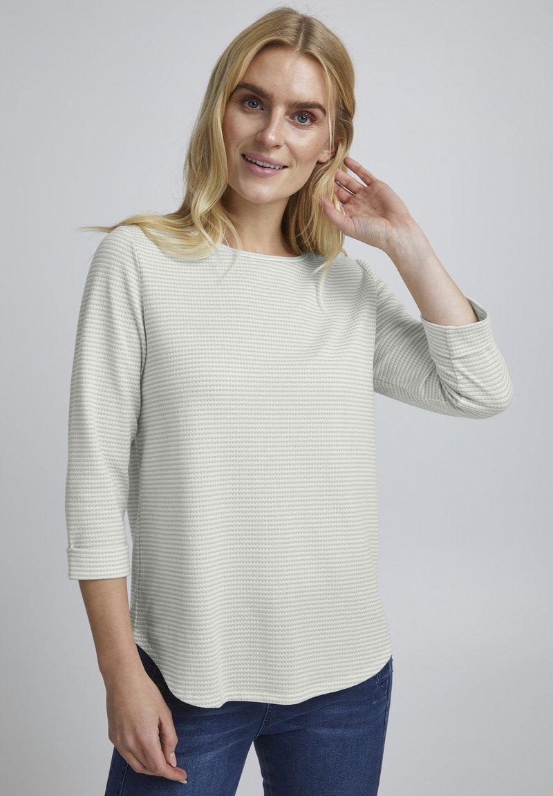 Helles graues, strukturiertes Shirt mit Dreiviertelärmeln, Rundhalsausschnitt und einem leicht abgerundeten Saum, kombiniert mit blauen Jeans.