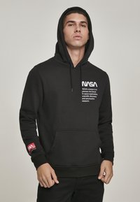 Haut à capuche noir en tissu doux, avec une poche avant, un cordon de serrage pour la capuche, le logo de la NASA et le texte de mission en blanc sur la poitrine, accent rouge sur la manche.