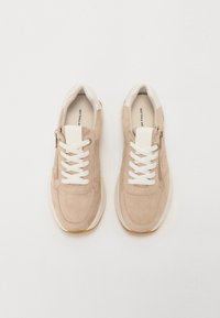 Baskets en suède beige avec lacets blancs, bout arrondi et fermeture éclair sur le côté. Accents blancs sur la languette et le talon, semelle texturée.