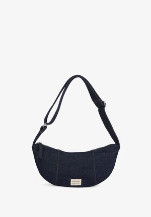 Sac à bandoulière en denim bleu foncé avec bandoulière réglable, fermeture éclair et une petite étiquette rectangulaire au centre en bas.