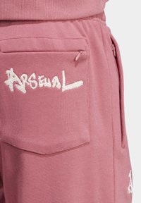 Rosa Jogginghosen mit gesticktem "Arsenal"-Logo, seitlichen Taschen und einer weichen Textur sowie einem elastischen Bund für zusätzlichen Komfort.