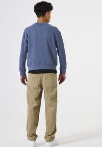 Blauwe katoen sweatshirt met ribbelboorden en zoom, gecombineerd met beige corduroy broek met twee achterzakken. Witte sneakers maken de look compleet.