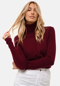 Burgundy polo tröja gjord av mjukt, texturerat tyg med långa ärmar, tillsammans med ljusa jeans som framhäver den avslappnade stilen.