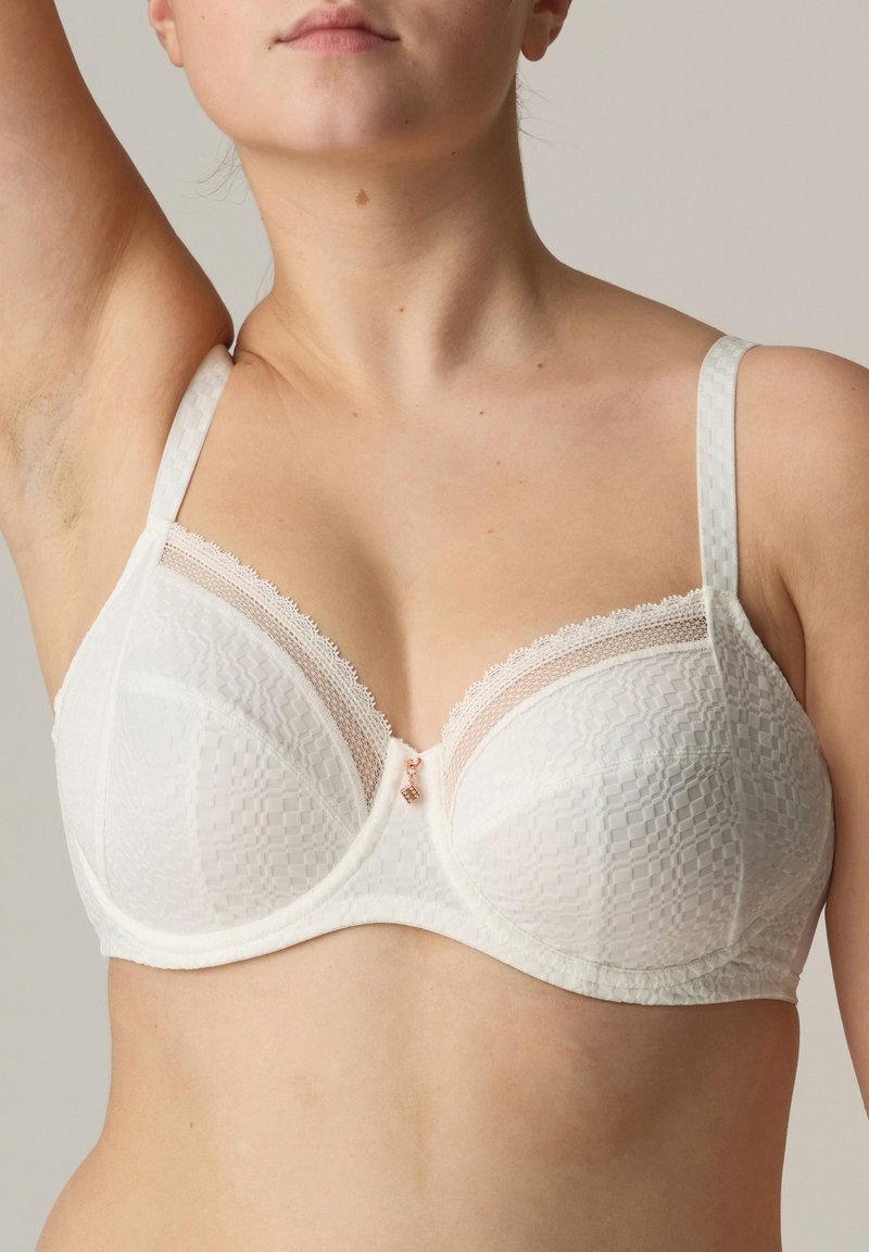 White bra featuring a textured fabric with a checkered pattern, sheer mesh panels, lace accents, and adjustable straps with decorative hardware.