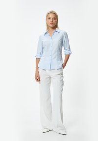 Lichtblauw overhemd met opgerolde mouwen, slim fit ontwerp. Gecombineerd met witte wijde broek en puntige hakken. Minimalistische stijl.